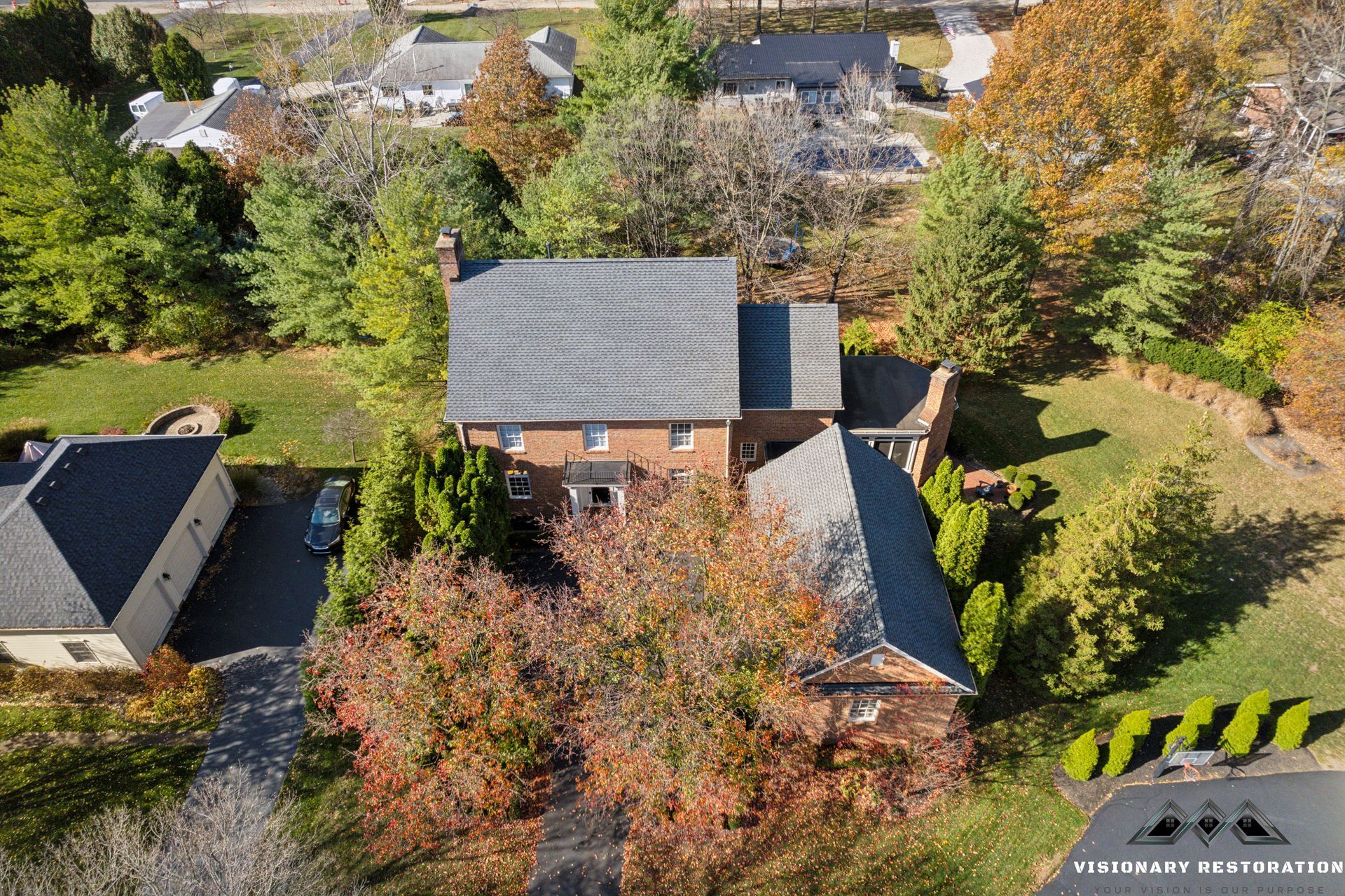 Aerial view of a two-story brick house with a dark gray roof surrounded by trees and a lawn.