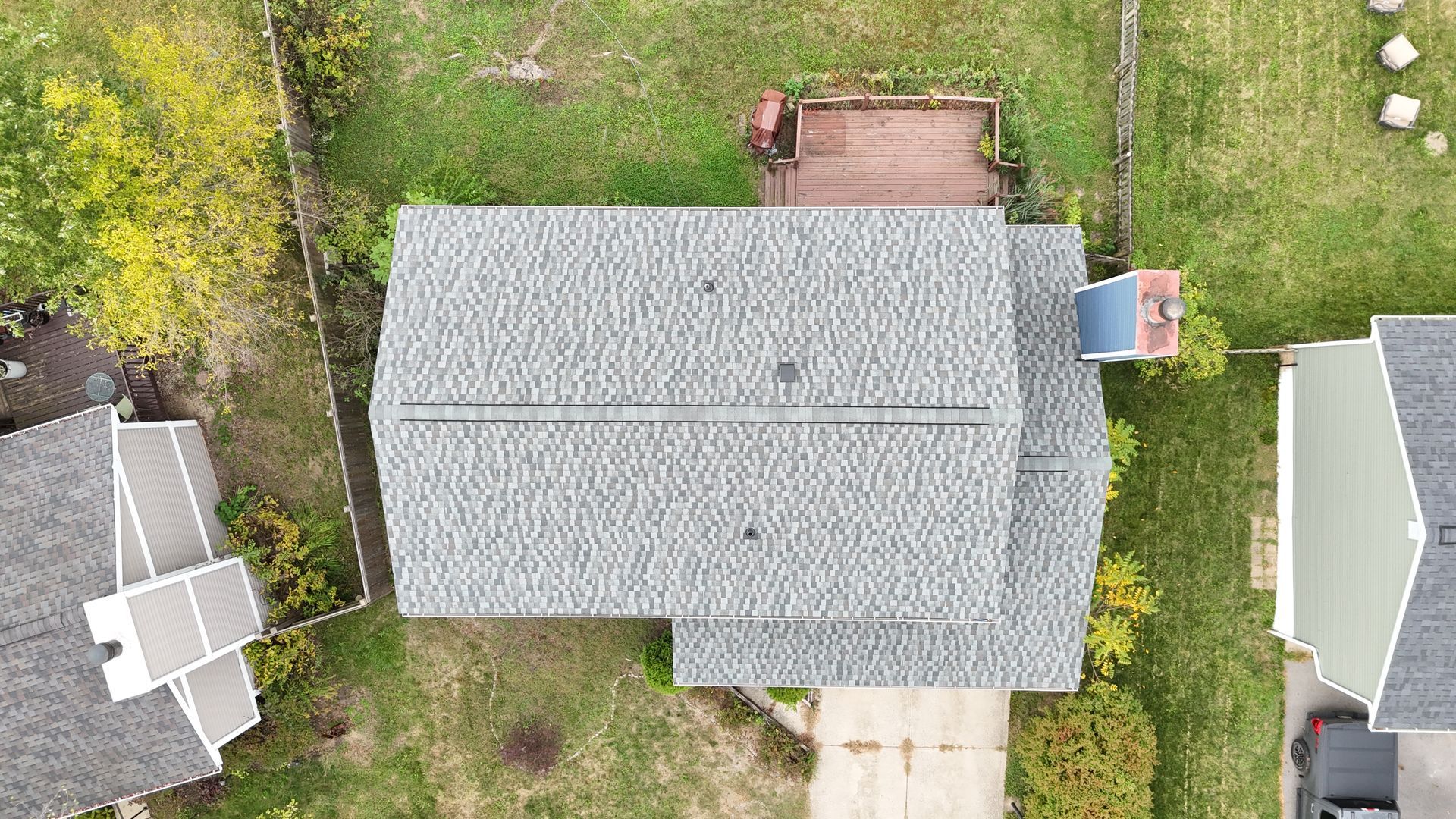 Overhead view of a house with a gray shingled roof, chimney, and surrounding yard with grass and trees.