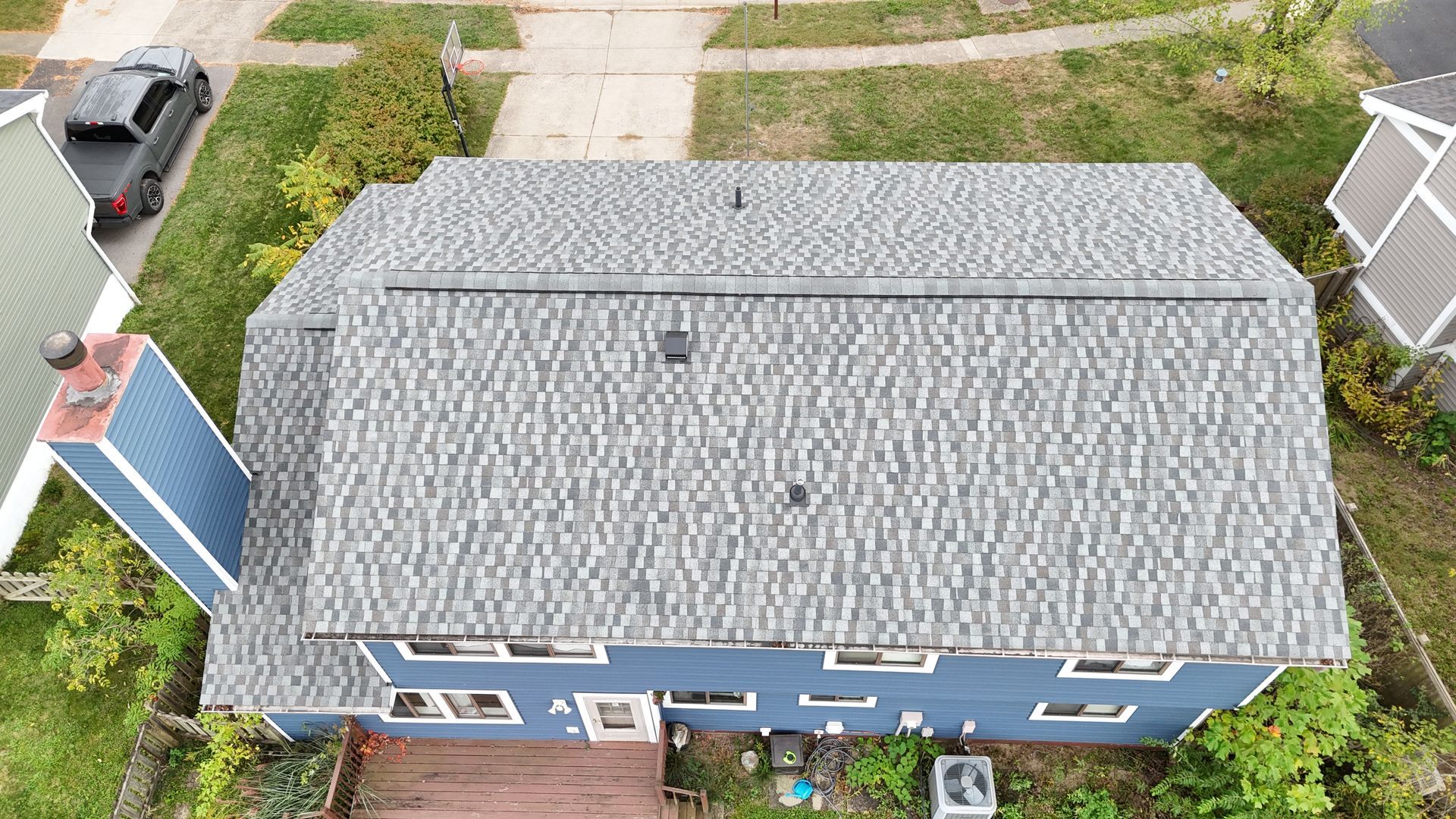 Aerial view of a blue house with gray roof shingles. A chimney and an SUV are visible.