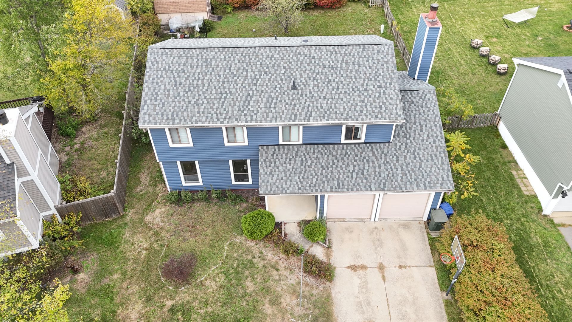 Blue two-story house with gray roof, concrete driveway, and surrounding green lawn.