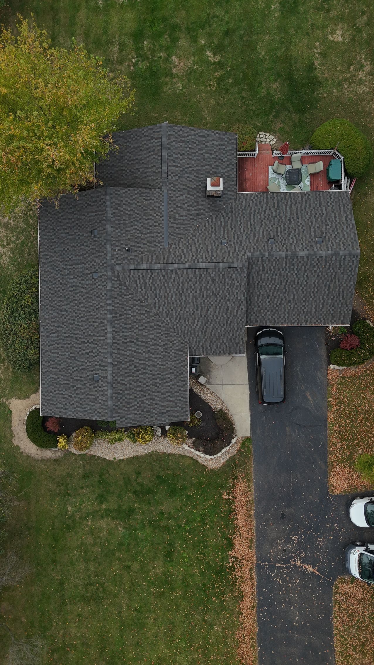 Overhead view of a house with a dark roof and driveway. A black car is parked in the driveway. Green lawn surrounds the house.