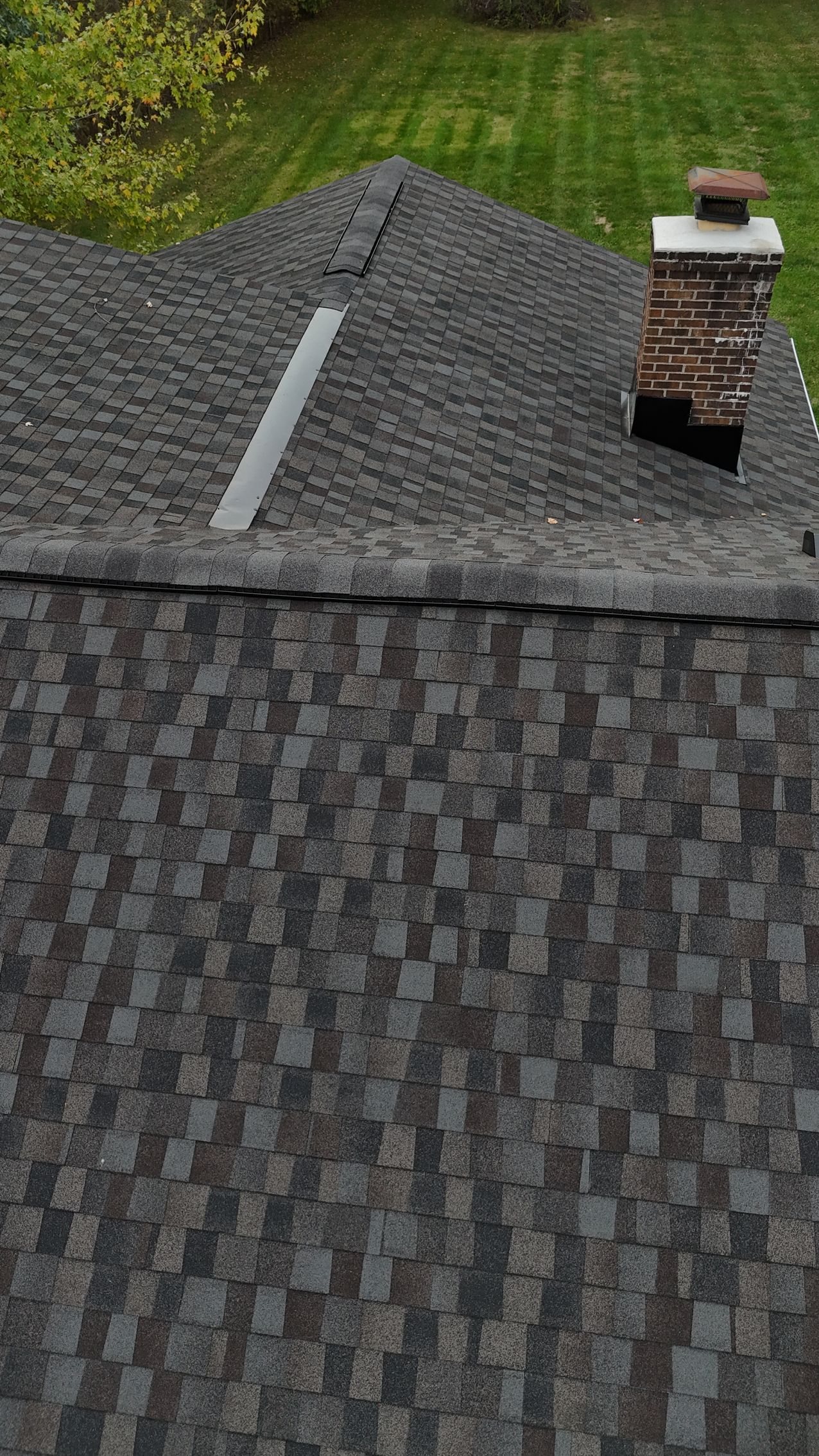 Overhead view of a dark gray asphalt shingle roof with a brick chimney and metal flashing.