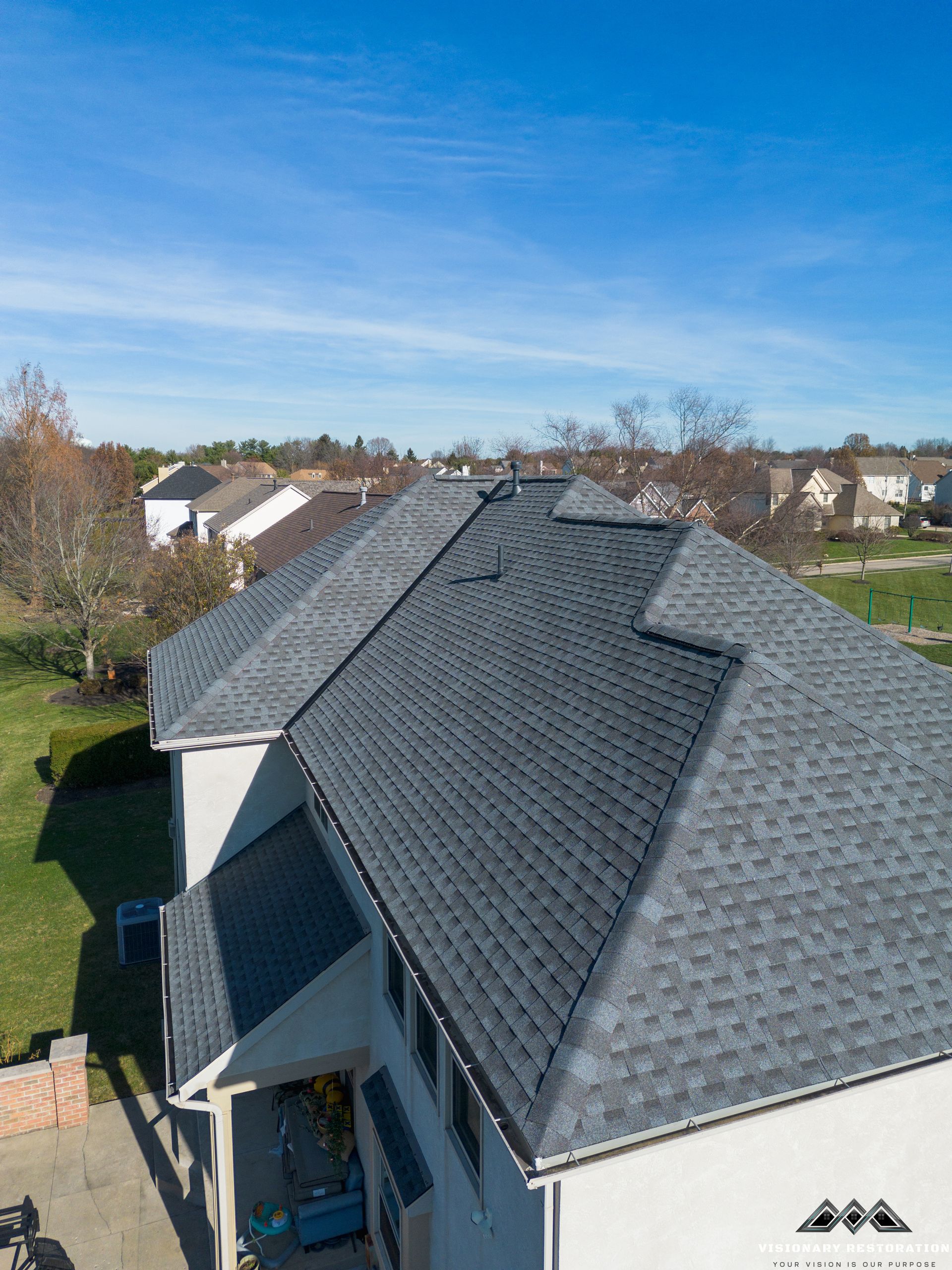 Aerial view of a house with a dark gray asphalt shingle roof against a clear blue sky.