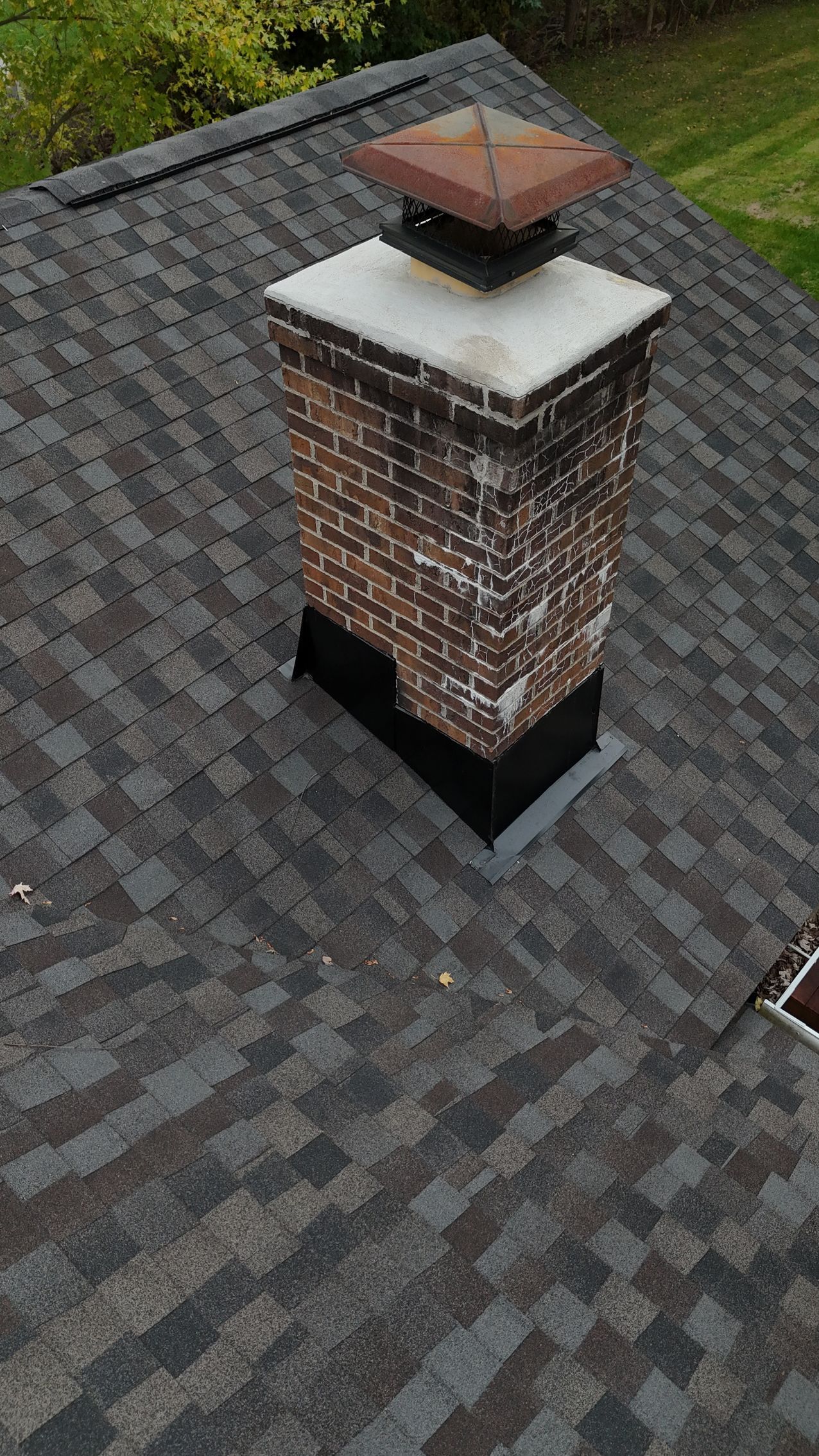 Brick chimney on a shingle roof, with a metal cap.