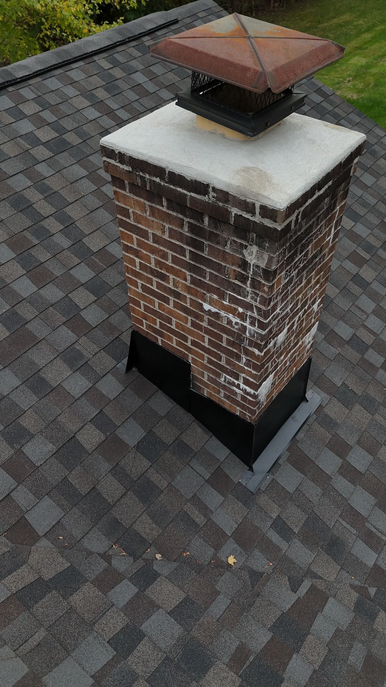 Brick chimney with a metal cap on a shingled roof.