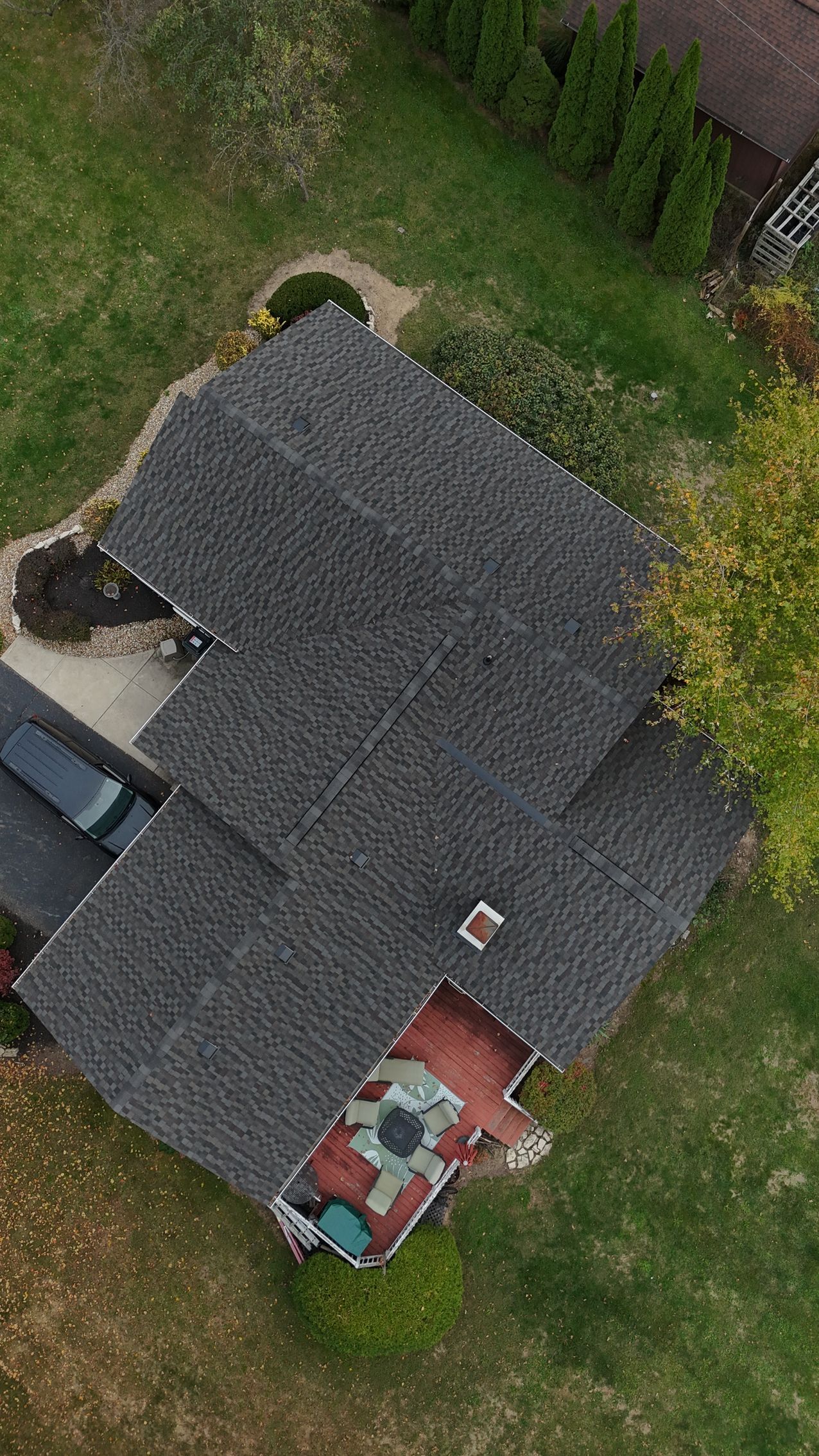 Aerial view of a house with gray shingles and red patio. Green lawn surrounds the house.