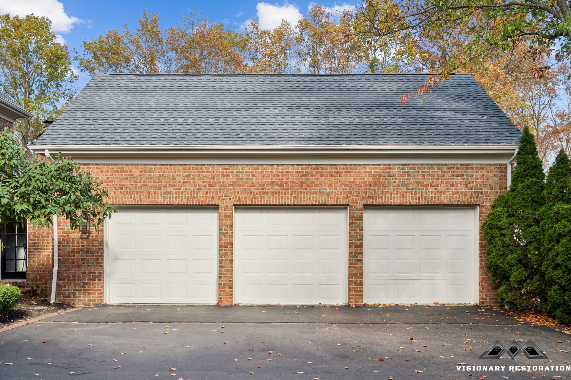 Three-car garage with white doors and gray shingle roof, made of brick.