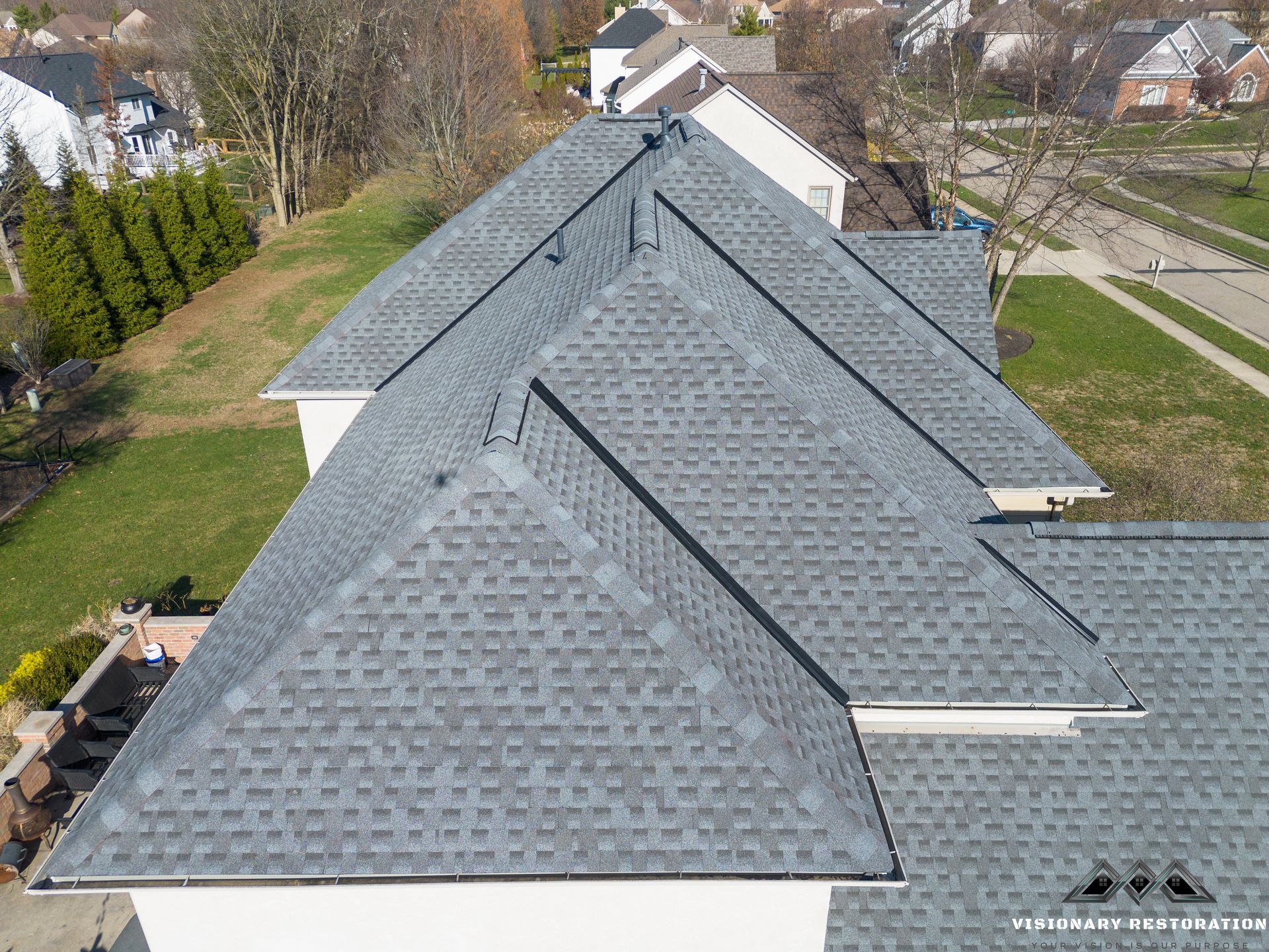Gray shingled roof of a house with multiple sections; aerial view, daytime.