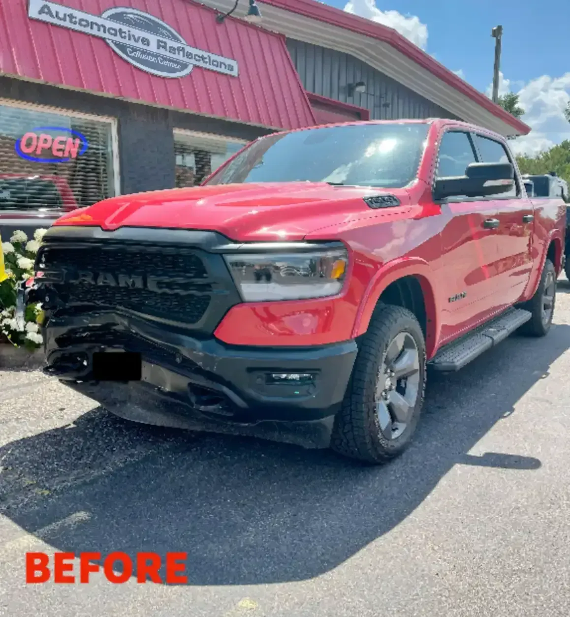 A damaged red Ram pickup truck parked in front of an automotive repair shop with the word 