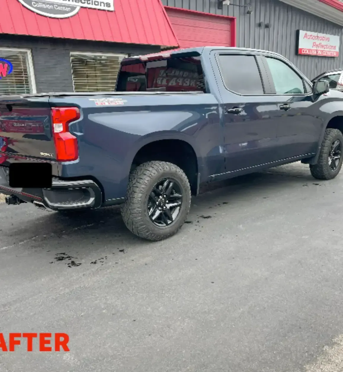 A dark blue pickup truck parked outside an automotive building with red accents, viewed from the rear quarter angle.
