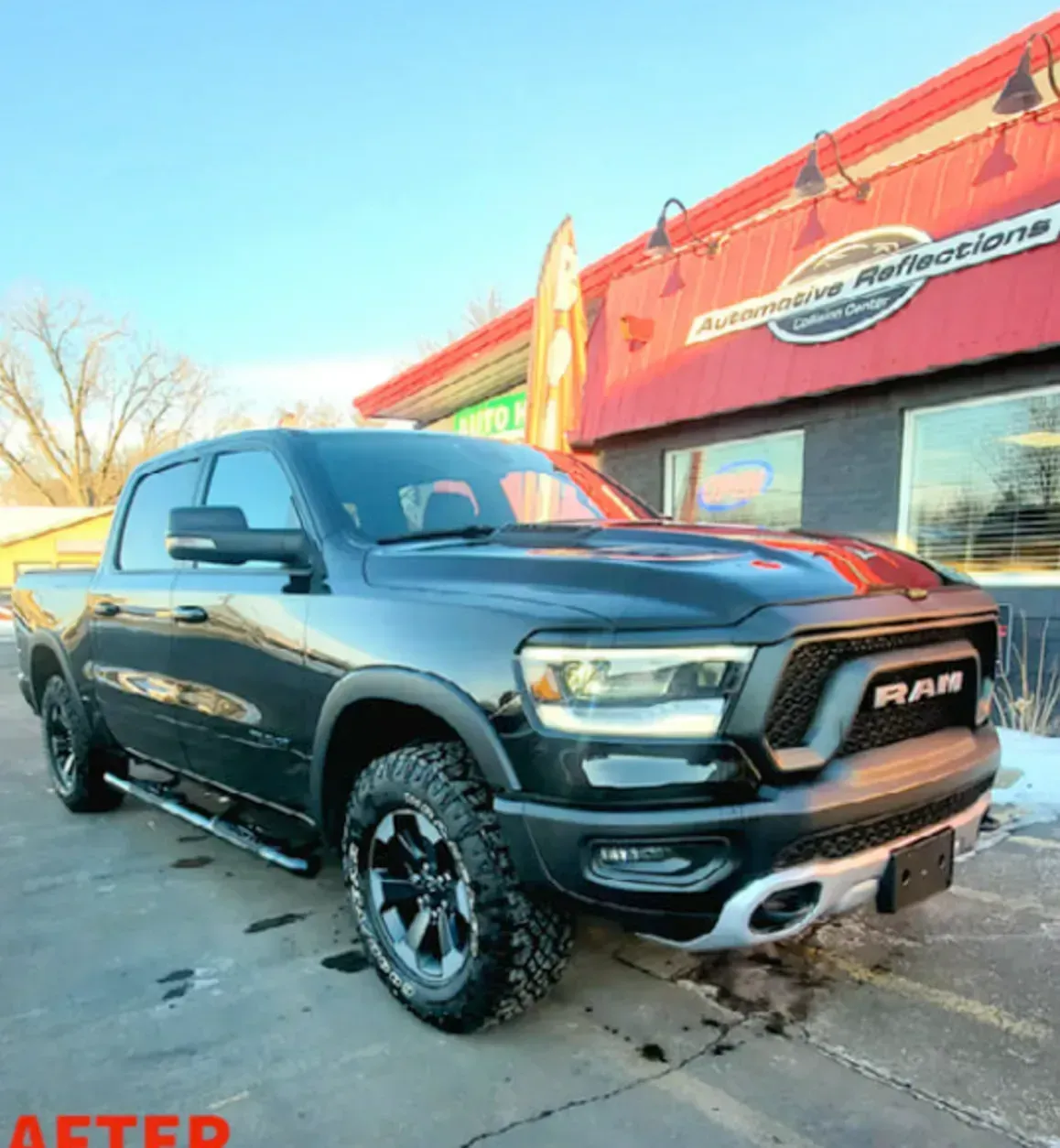 A dark gray Ram pickup truck parked in front of an automotive business on a sunny day.