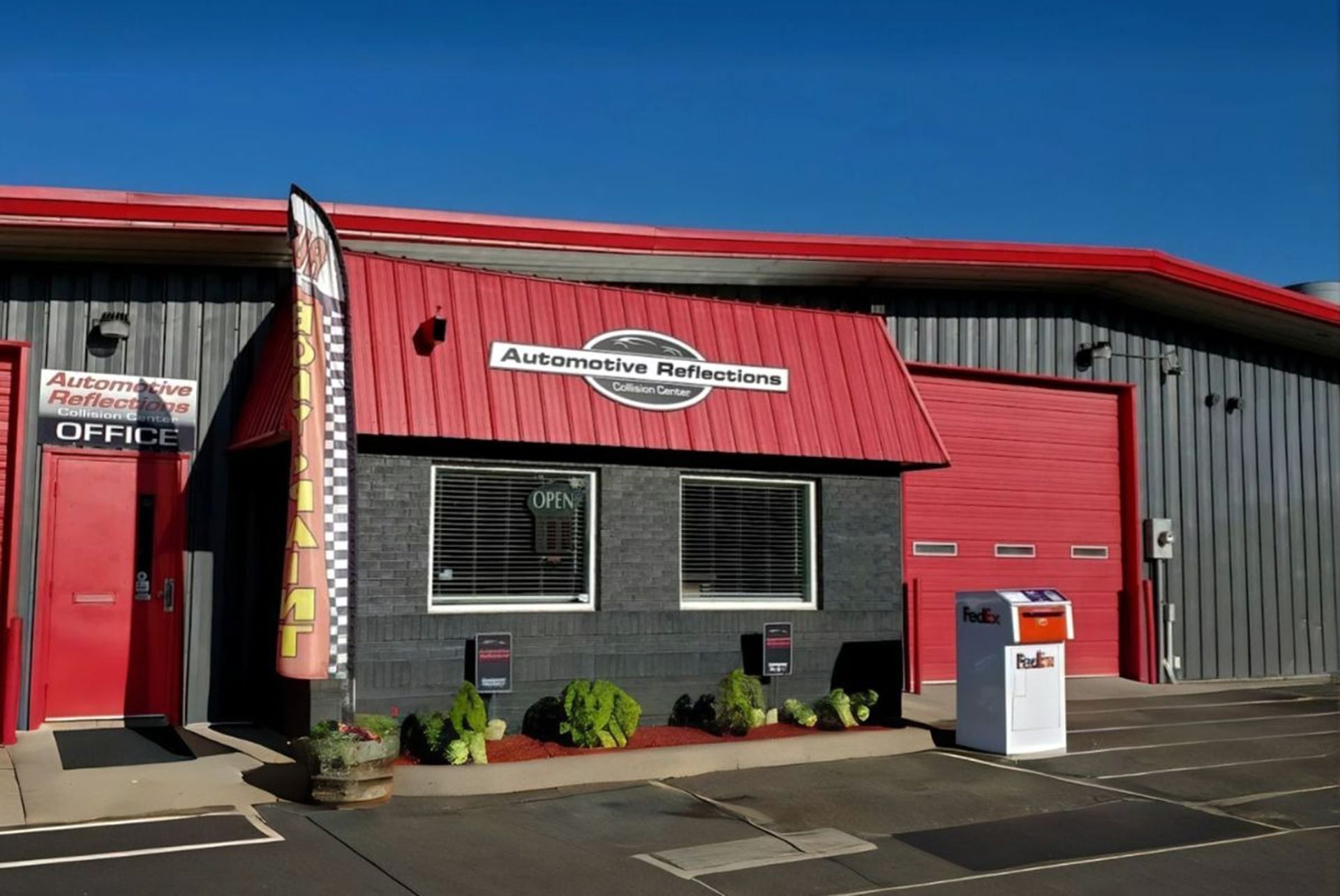 Automotive Refinishing shop with a red roof, black brick exterior, and red doors under a clear blue sky.