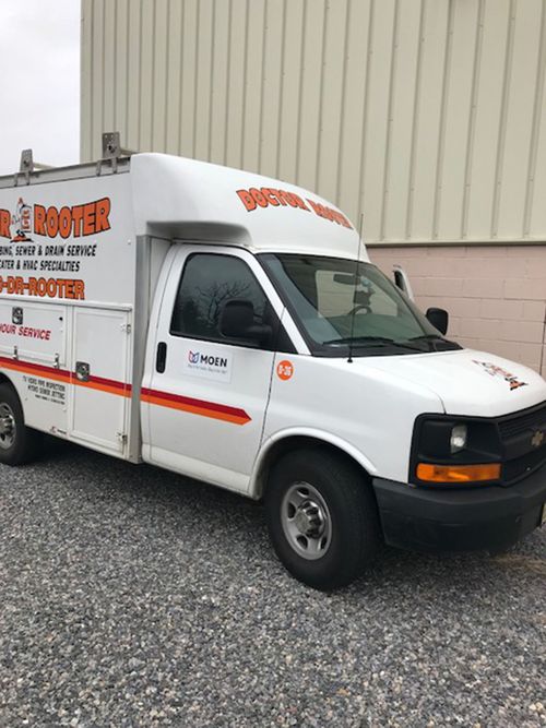 White service van with orange lettering parked outside a beige building on gravel.