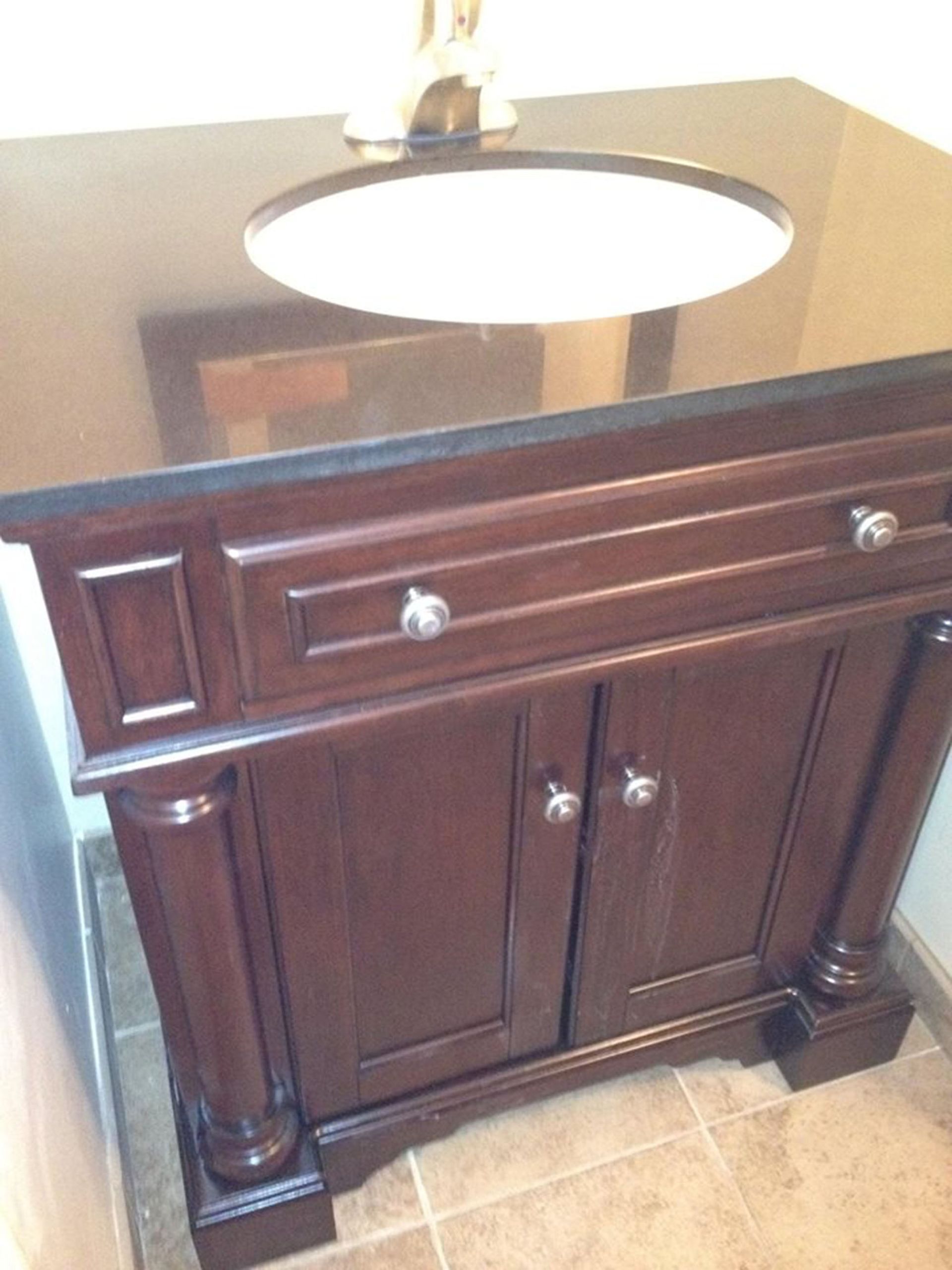 Dark wooden bathroom vanity with oval sink and mirrored countertop on tiled floor