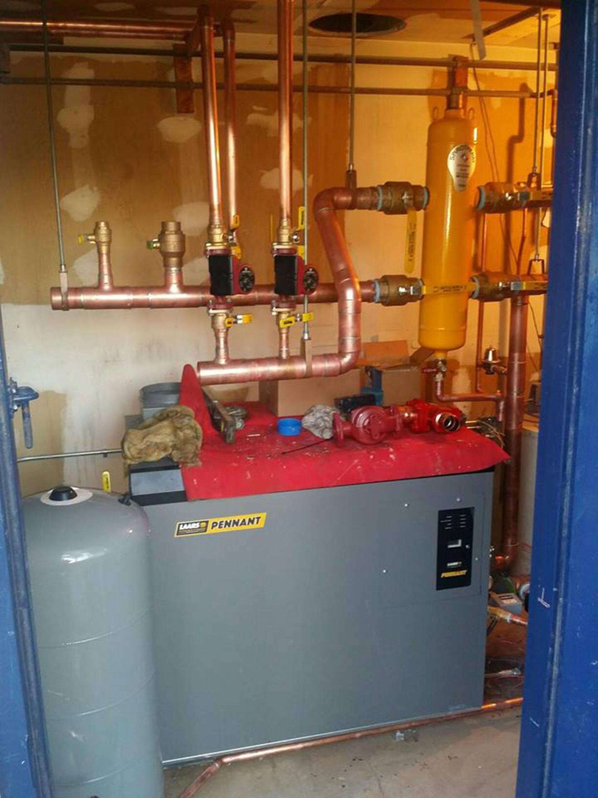 Large gray and red boiler with copper pipes in a utility room