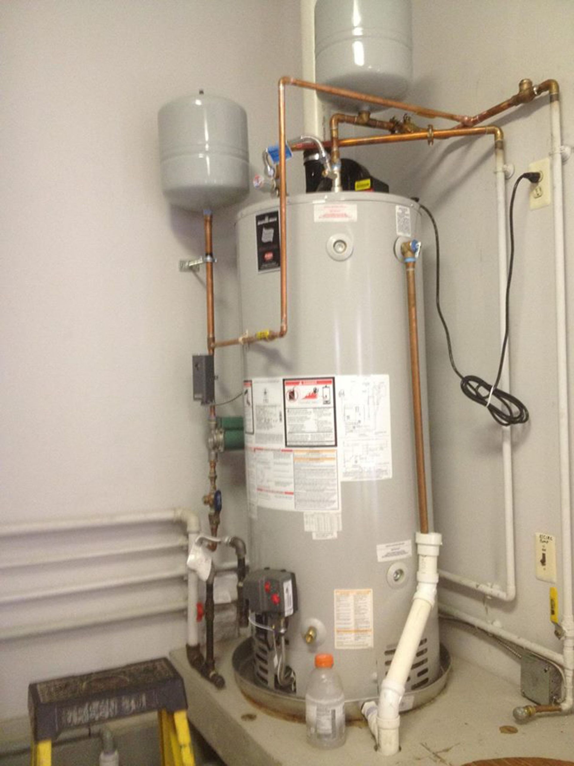 Water heater and plumbing equipment in a utility room, with copper pipes and a gray expansion tank.
