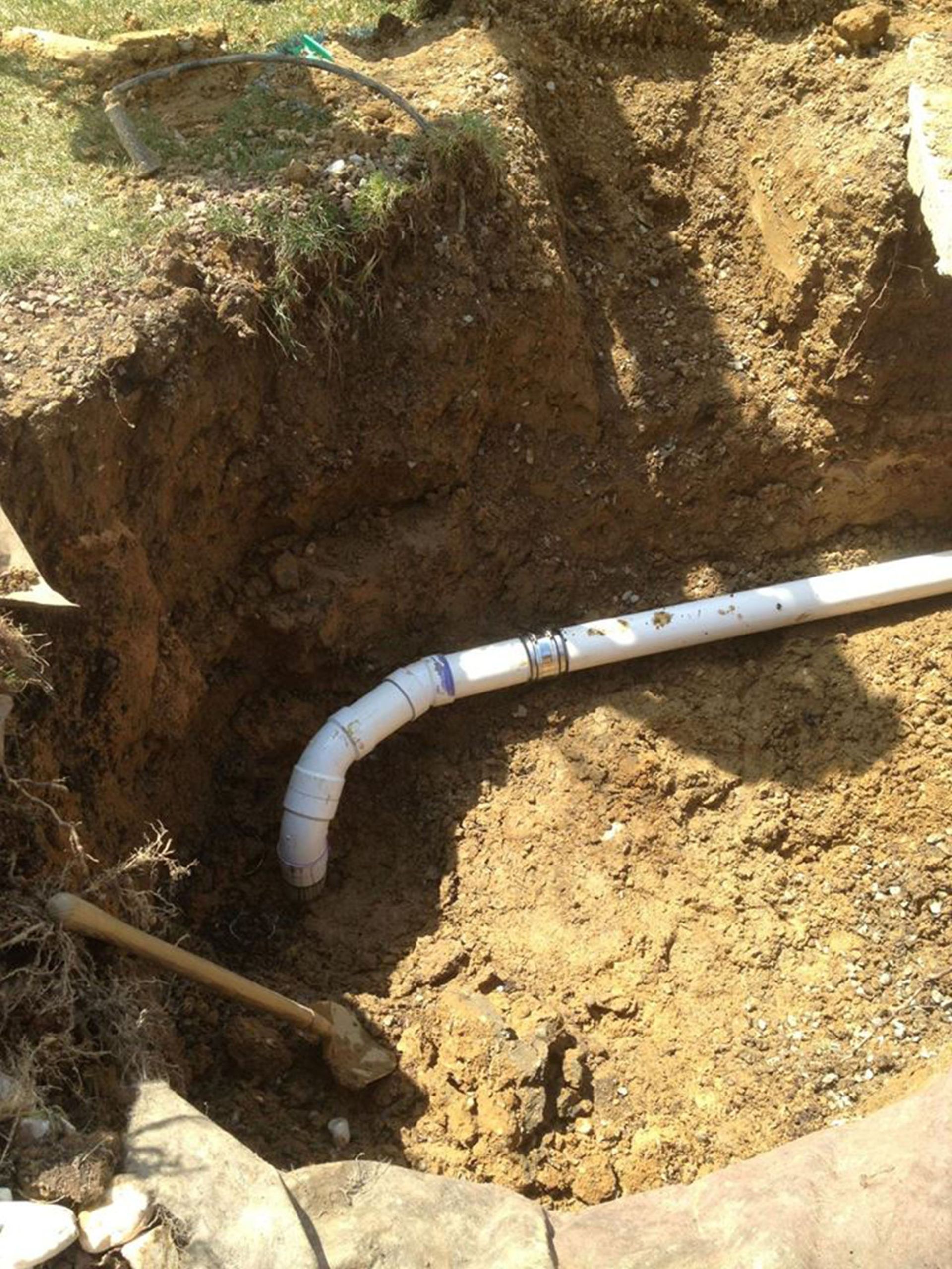 Dug-out trench with a white PVC pipe bending through dirt near a grassy edge