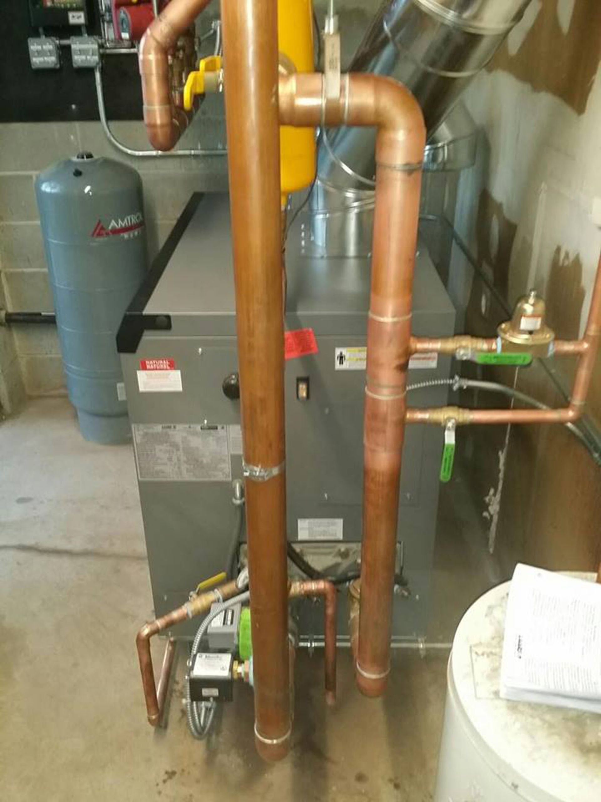 Copper pipes and HVAC equipment in a mechanical room, with a gray unit and ductwork in the background.