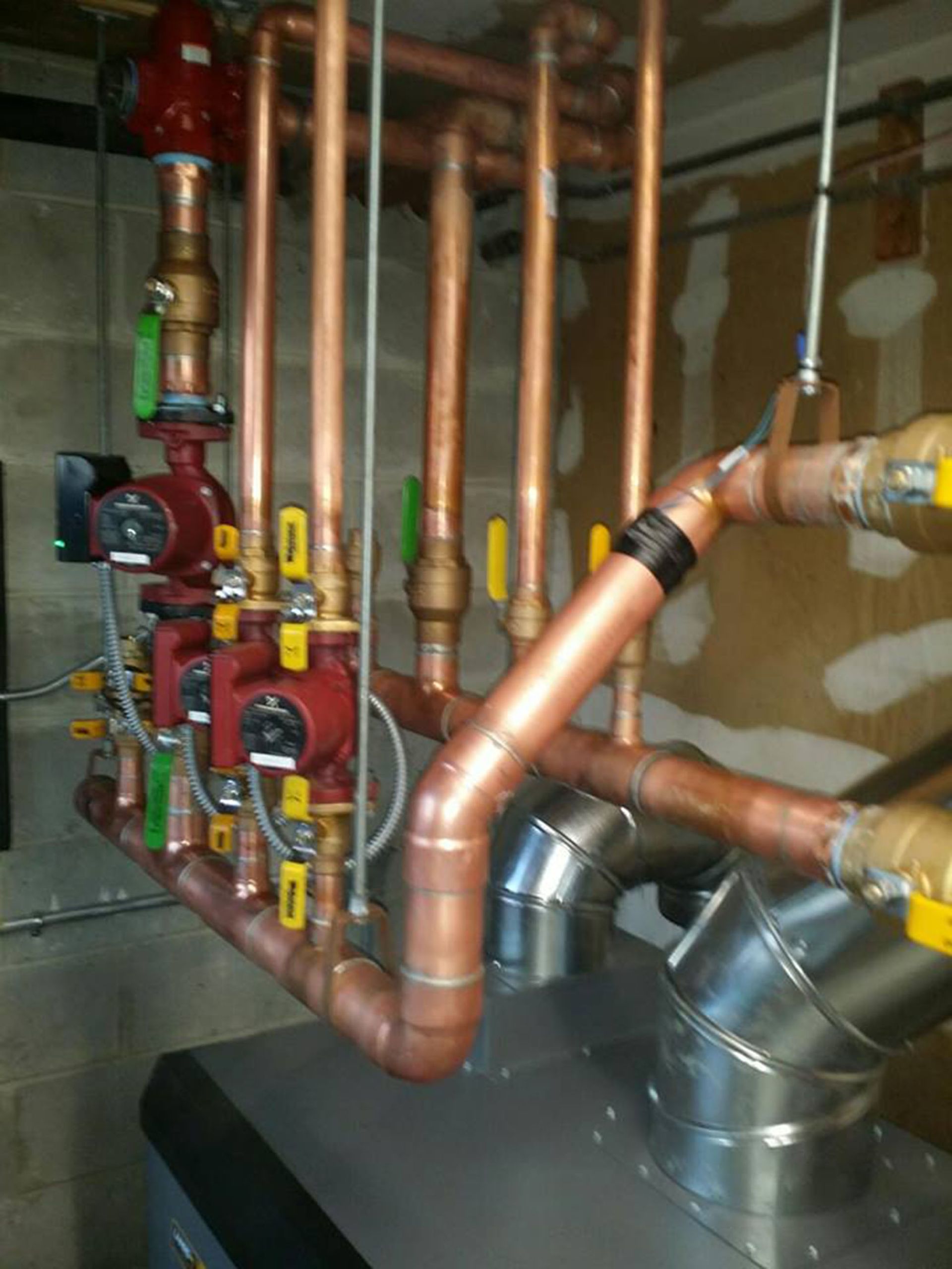 Copper pipes and red valves in a mechanical room, with metal ductwork and unfinished walls.