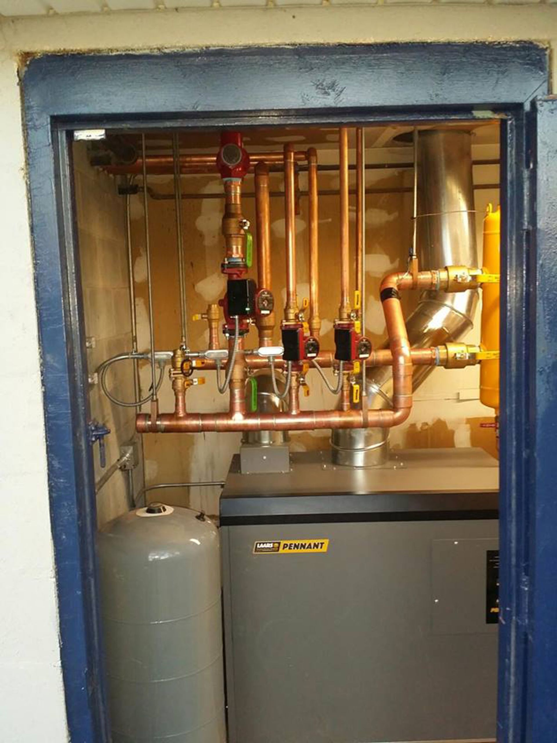 Boiler room with copper pipes, valves, and gray equipment inside a utility closet.