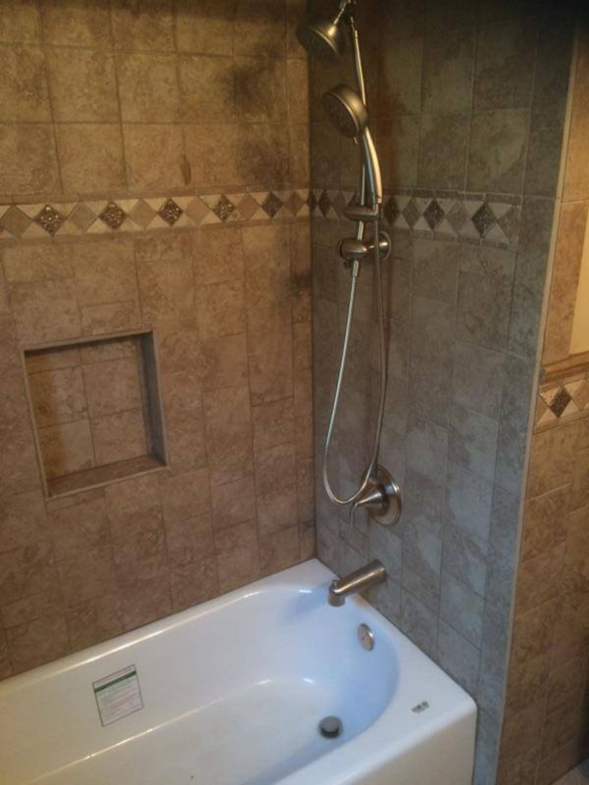 Bathroom tub and shower with beige tiled walls and a handheld showerhead above the tub.