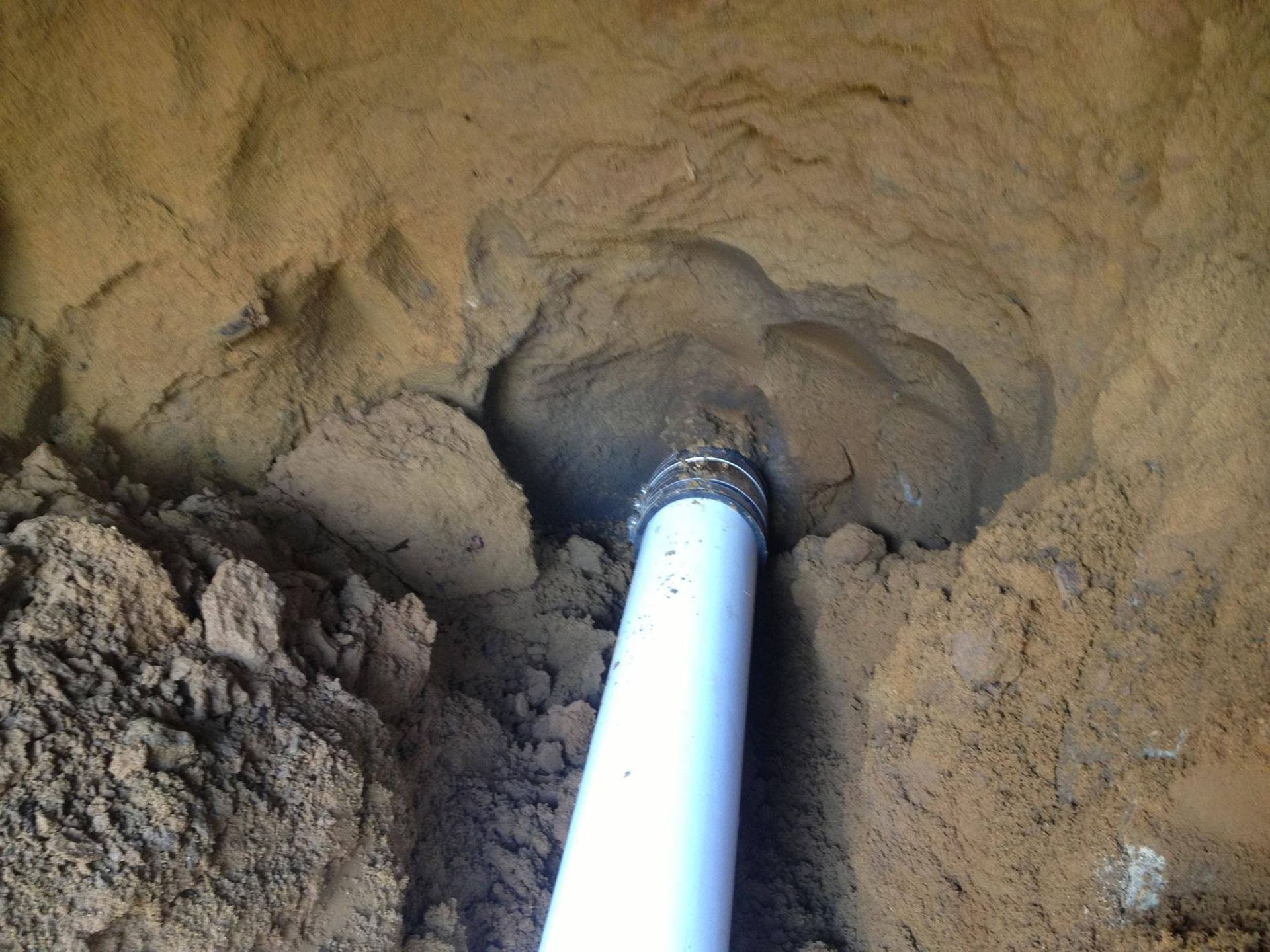 White pipe inserted into a dirt wall inside a dug hole or trench