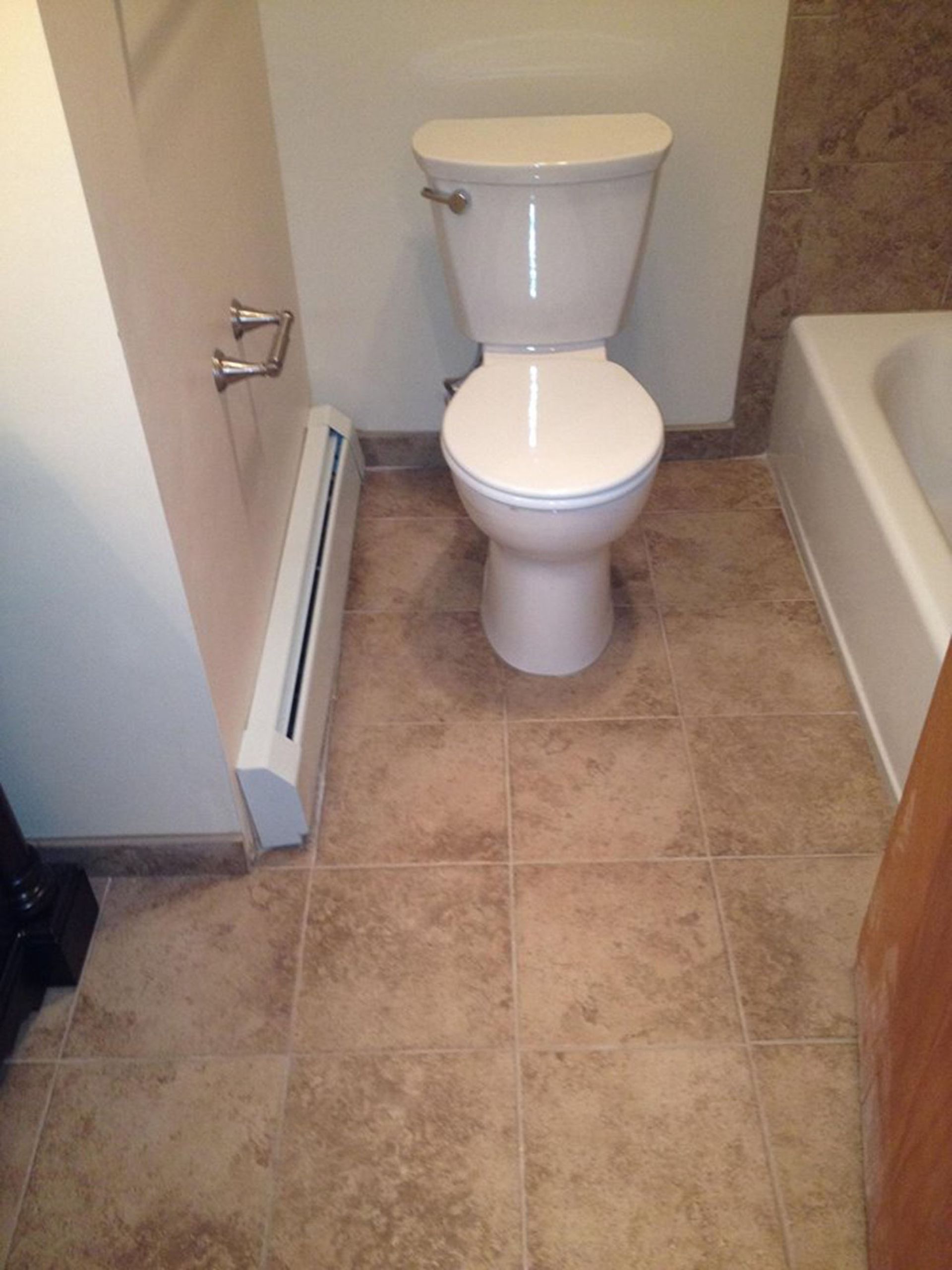 Small bathroom with a white toilet beside a bathtub and beige tiled floor.