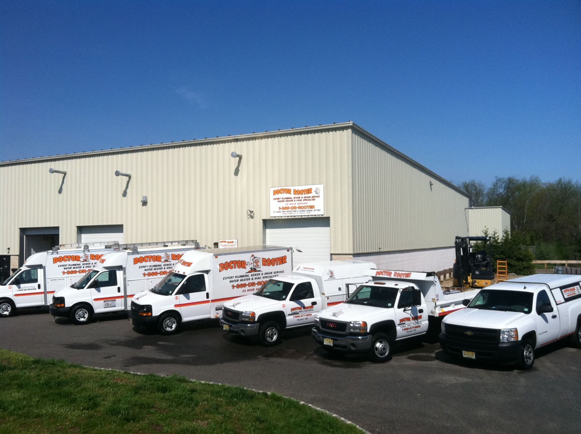 White trucks and vans parked outside a beige industrial building on a sunny day