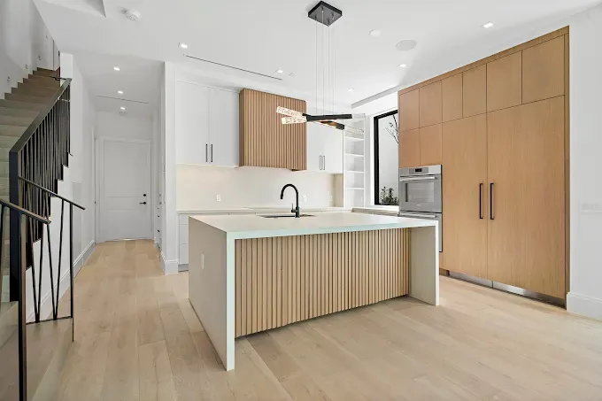 Modern kitchen with light wood cabinets, white countertops, and a central island.