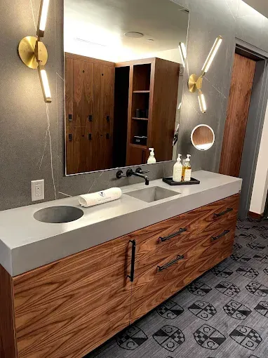 Modern bathroom with wooden vanity, concrete countertop, and lockers in the background.