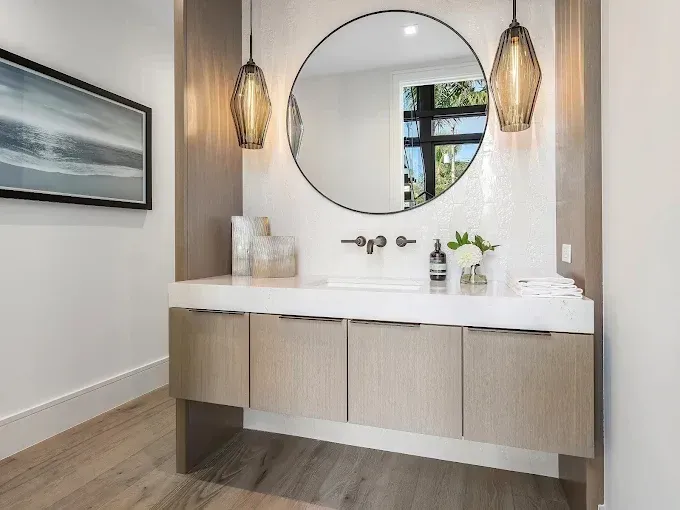 Powder room with a round mirror, wood vanity, and two pendant lights.
