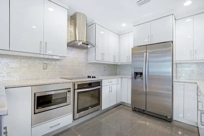 White modern kitchen with stainless steel appliances and glossy cabinets.