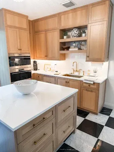 Modern kitchen with light wood cabinets, white countertops, and a checkered floor.