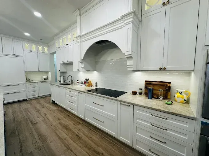 White kitchen with wood floors, white cabinets, range hood, and granite countertops.