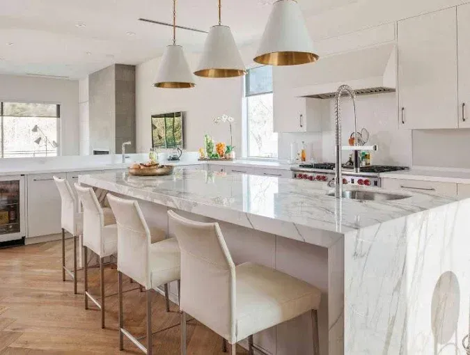 Modern kitchen with a marble island, bar stools, and pendant lights.