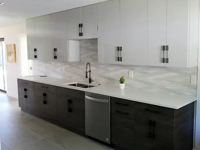 Modern kitchen with white upper cabinets and dark lower cabinets, with white countertops and a stainless steel dishwasher.