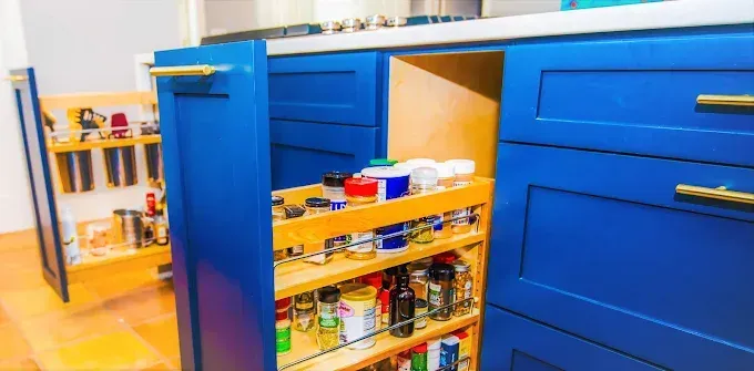 Blue kitchen cabinets with pull-out spice racks. Golden handles and light wooden interior.