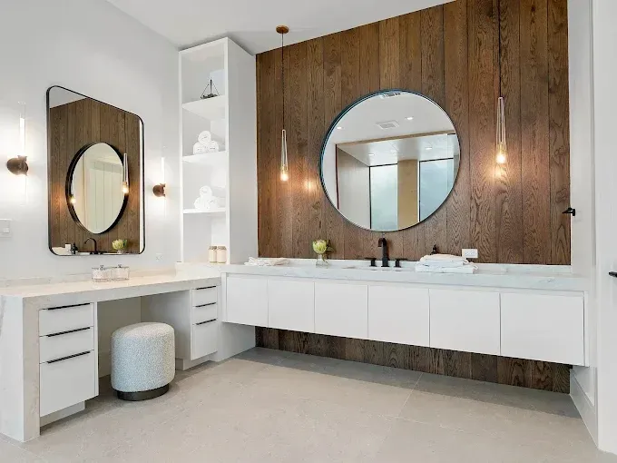 Modern bathroom with white vanity, wooden accent wall, and large round mirror.