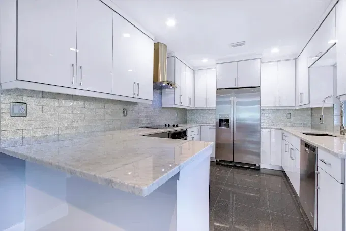 White kitchen with stainless steel appliances, white cabinets, and marble countertops.