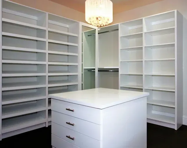 White walk-in closet with shelves, a center island with drawers, and a chandelier.