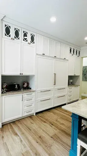 White kitchen cabinets and refrigerator with wood floor and blue island.