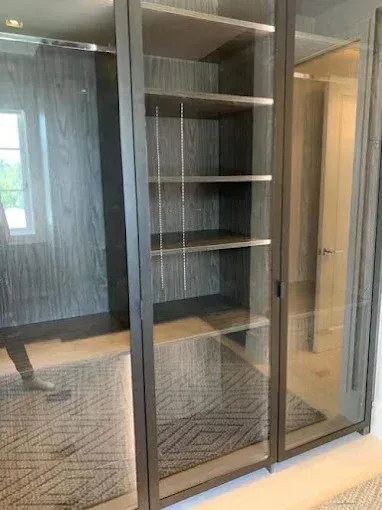 A built-in cabinet with glass doors and shelves inside a walk-in closet with a patterned rug.