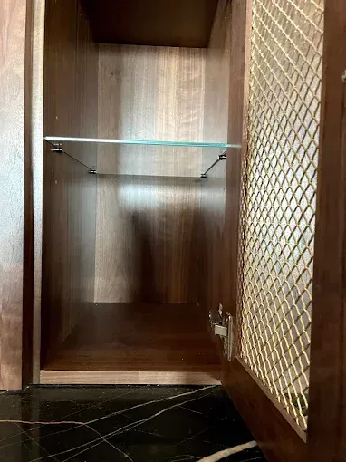Open wooden cabinet with glass shelf, metal mesh door, on black counter.