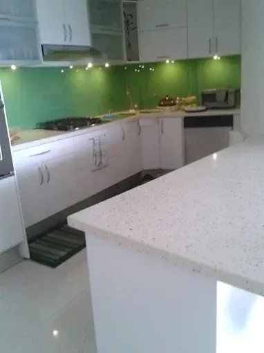White kitchen with quartz countertops, green backsplash, and white cabinets.