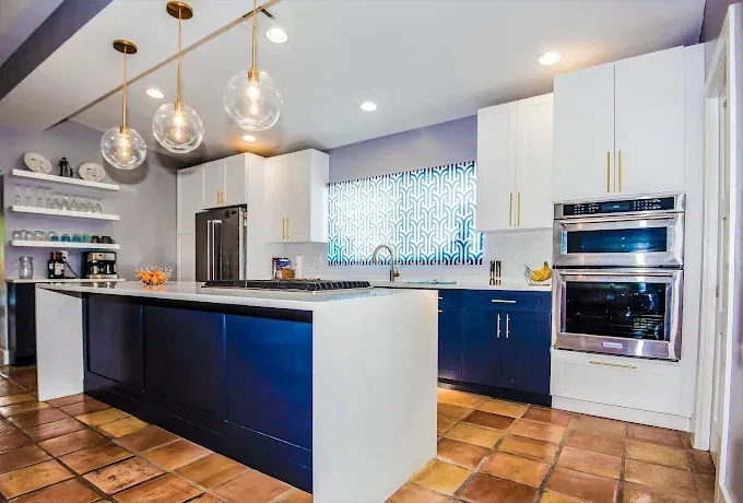 Modern kitchen with white and blue cabinets, island, stainless steel appliances, and globe pendant lights.