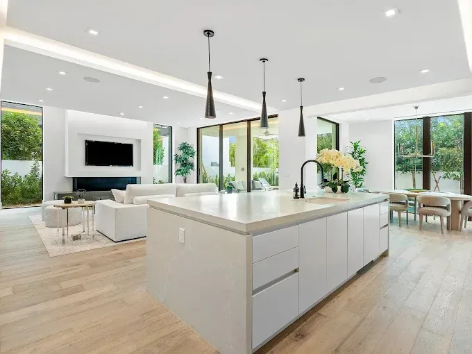 Modern kitchen with island, open to living area, light wood floors, white walls and furniture.