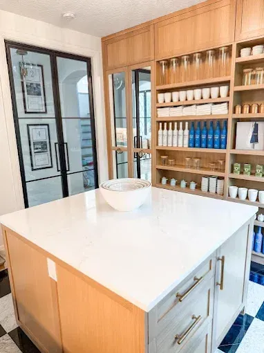 Kitchen pantry with a white island, wood shelving, and black-framed glass doors.