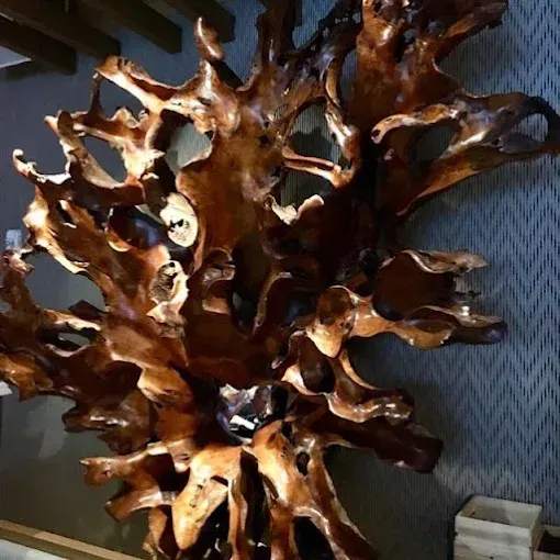 Abstract, brown, wooden sculpture against a textured, gray wall.