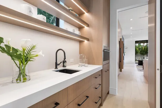 Modern kitchen area with wooden cabinetry, sink, open shelving, and hallway entrance.