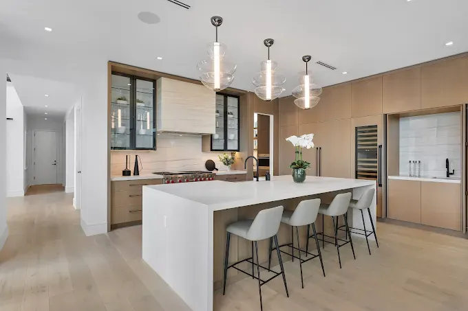 Modern kitchen with white island, gray stools, wood cabinets, and pendant lights.